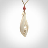 Hand carved bone hook pendant hand made by Peter Mitchell in New Zealand. This bone hook is provided with an adjustable Kalahari cord and packaged in a woven kete pouch. Free delivery worldwide.